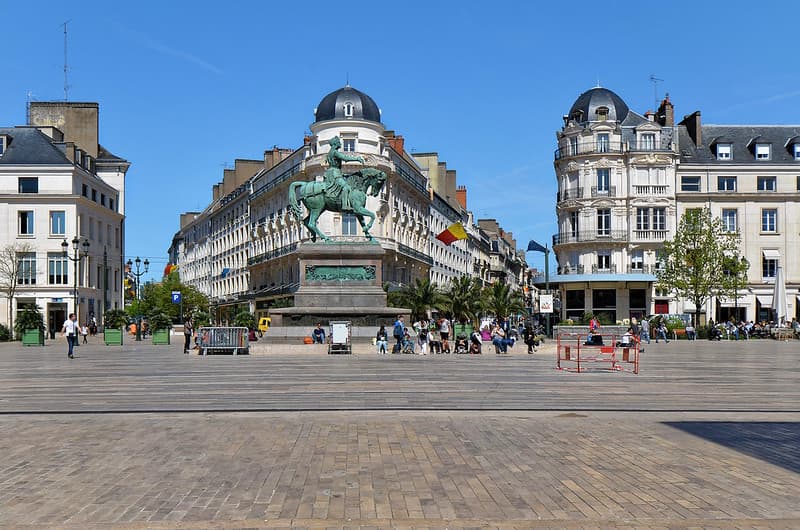 Place du Martroi à Orléans avec la statue équestre de Jeanne d'Arc au centre, entourée de bâtiments historiques et de passants.