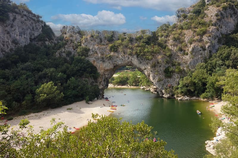 Pont d'Arc naturel en Ardèche, arche rocheuse surplombant une plage de sable et la rivière où naviguent des canoës et kayaks